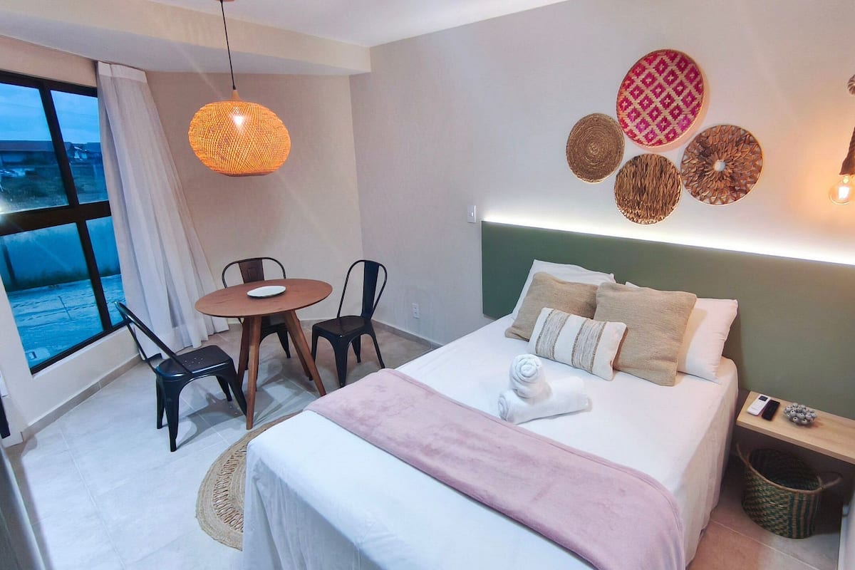 Ein Hotelzimmer mit Bett, Nachttisch, Lampe, Stuhl und Blick aus dem Fenster.
