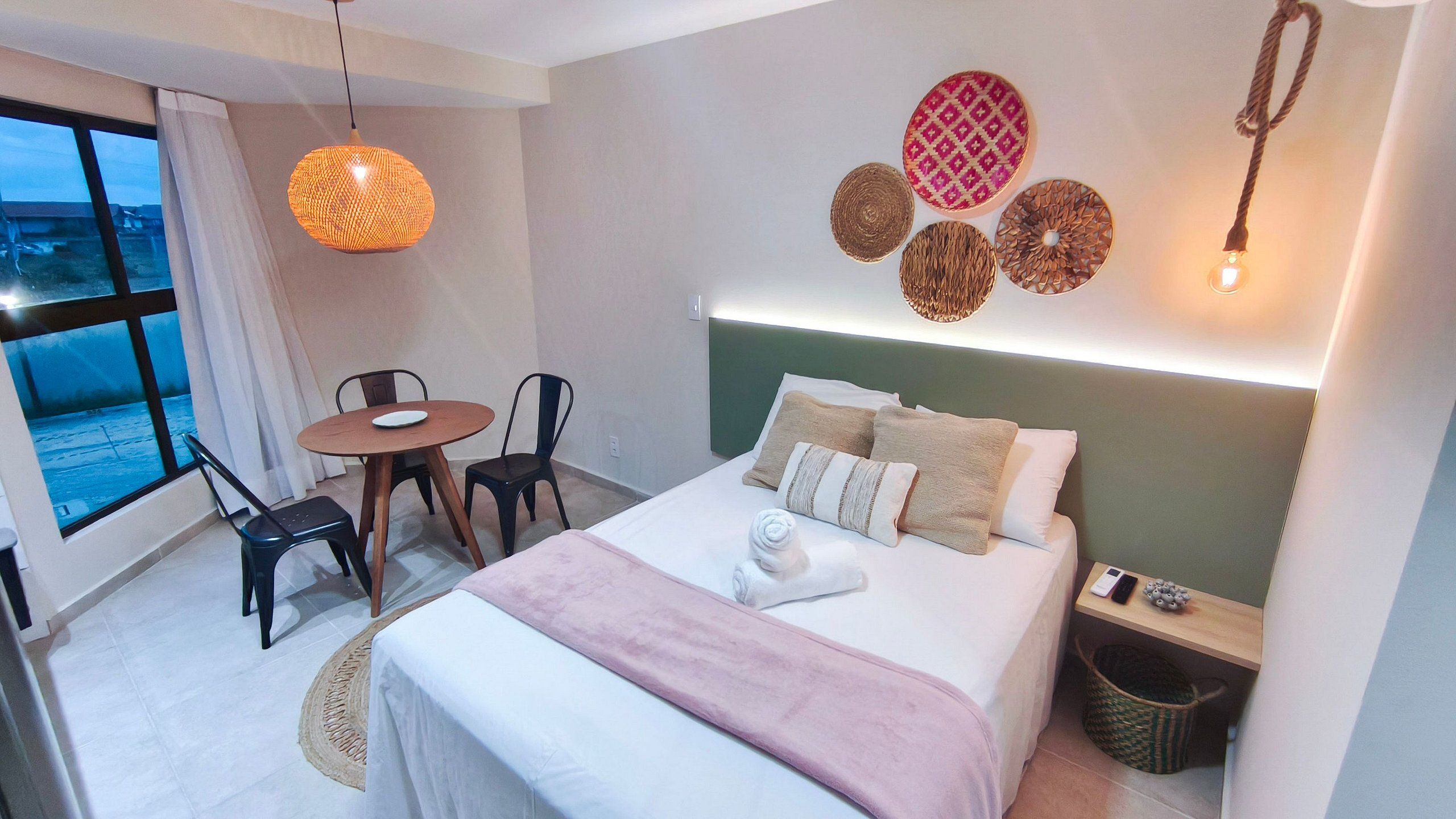 A hotel room with a bed, bedside table, lamp, chair, and a view through the window.