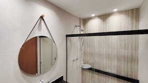 Une salle de bain moderne avec un miroir rond, une cabine de douche en verre et un lavabo à cadre noir.