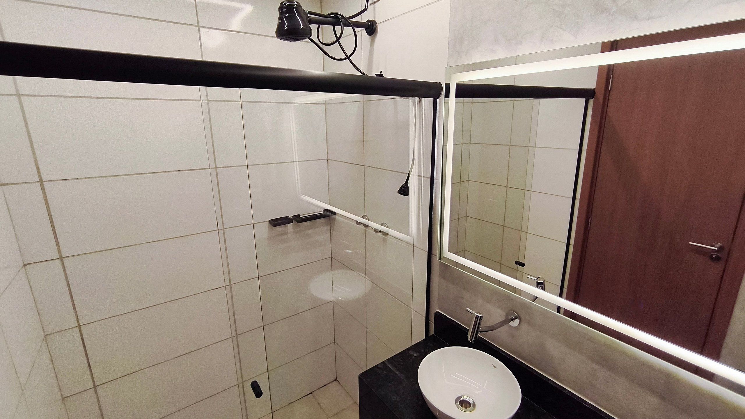 A bathroom with white tiled walls, a black countertop, a white sink, and a mirror.
