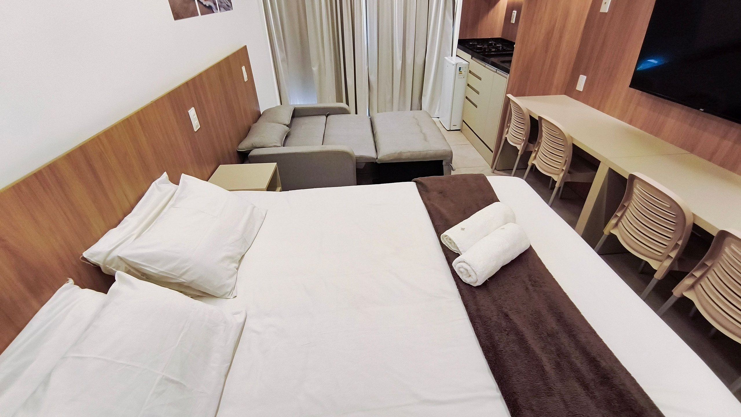 Une chambre d’hôtel comprenant un lit, un petit bureau, une chaise, une télévision et une kitchenette.