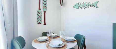 Un comedor con una mesa redonda preparada para cuatro personas, rodeada de sillas color turquesa, con un adorno de pez montado en la pared y dos tapices.