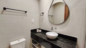 A bathroom with a white toilet, a black countertop, a white sink, a mirror, and a towel rack. - Max Carneiros Suites by CTA (Tamandaré)