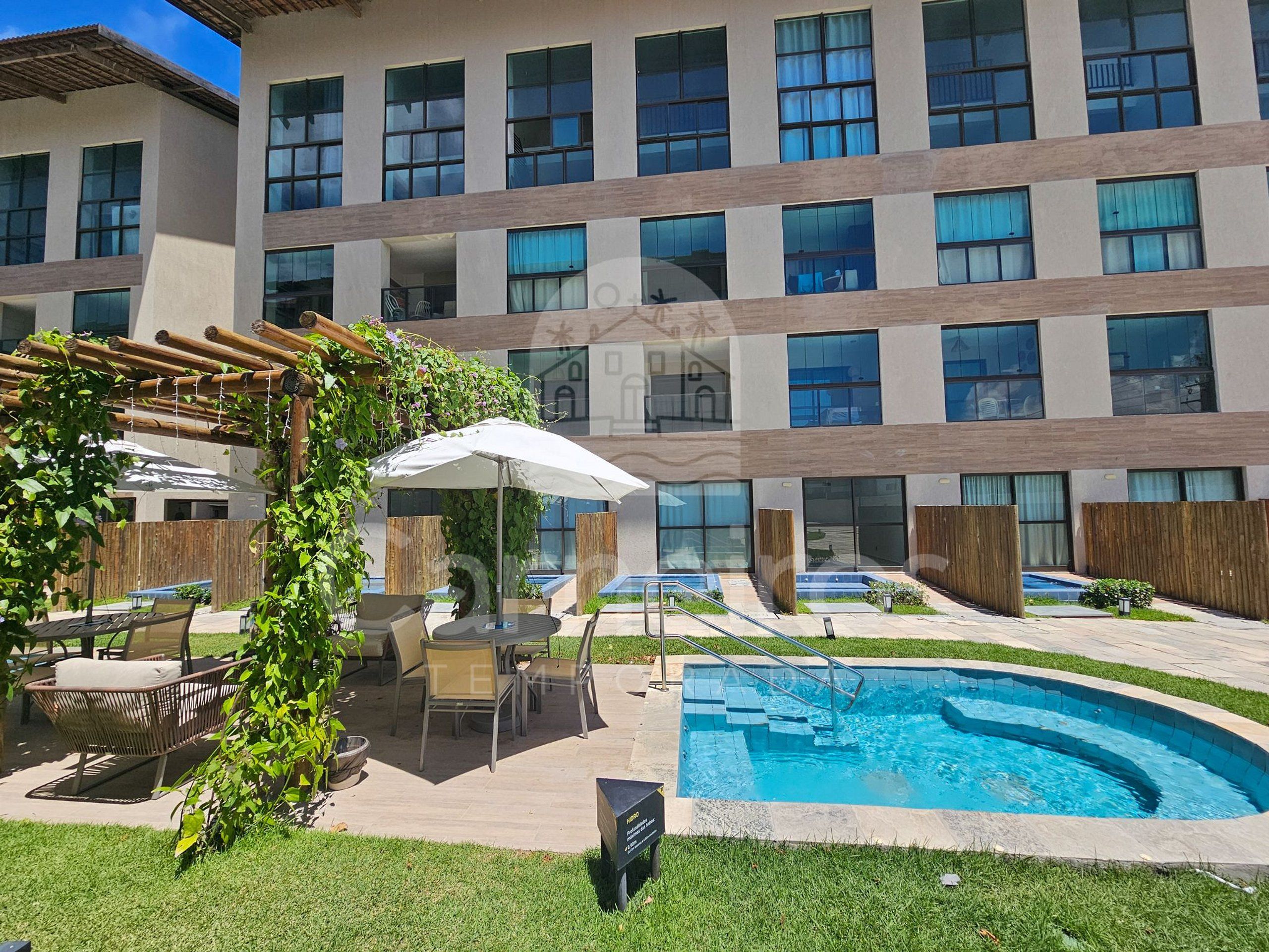 A hotel courtyard with a swimming pool, outdoor seating, and a pergola covered with greenery.