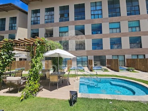 Une cour d’hôtel avec une piscine, des espaces de détente en plein air et une pergola recouverte de verdure.