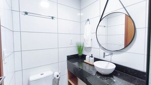A modern bathroom with white tiles, a round mirror, a white sink, a towel rack, and a toilet.
