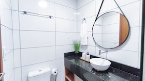 Une salle de bain moderne avec des carreaux blancs, un miroir rond, un lavabo blanc, un porte-serviettes et des toilettes.