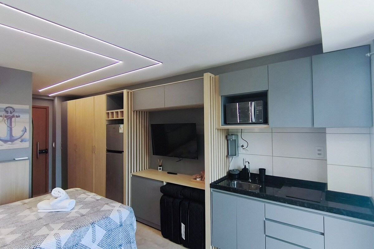 A compact hotel room with a bed, a TV, a kitchenette, and a wardrobe.