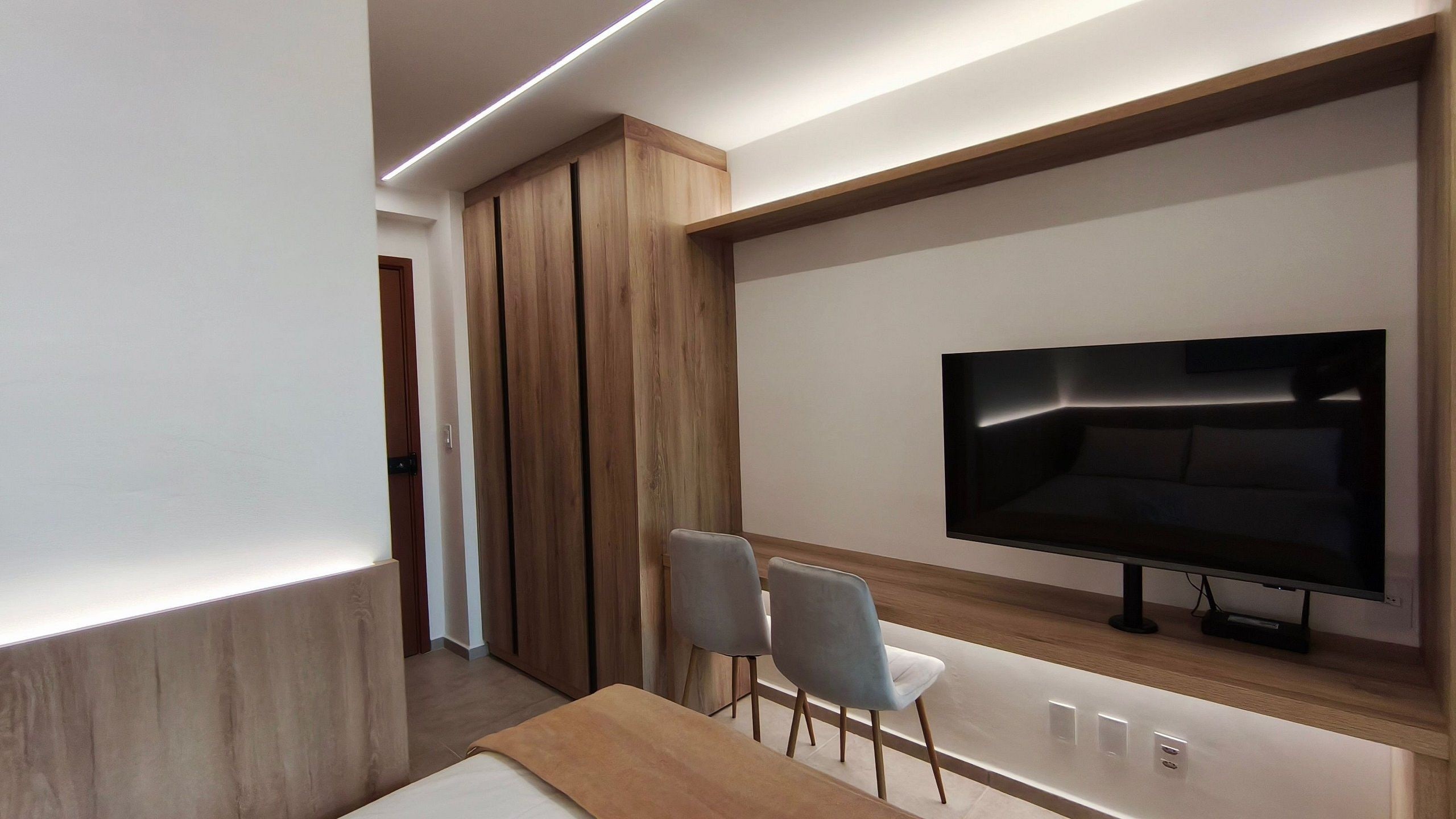 A modern living room with a flat-screen TV, wooden cabinets, and two grey chairs.