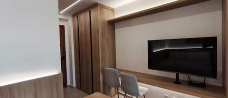 A modern living room with a flat-screen TV, wooden cabinets, and two grey chairs.