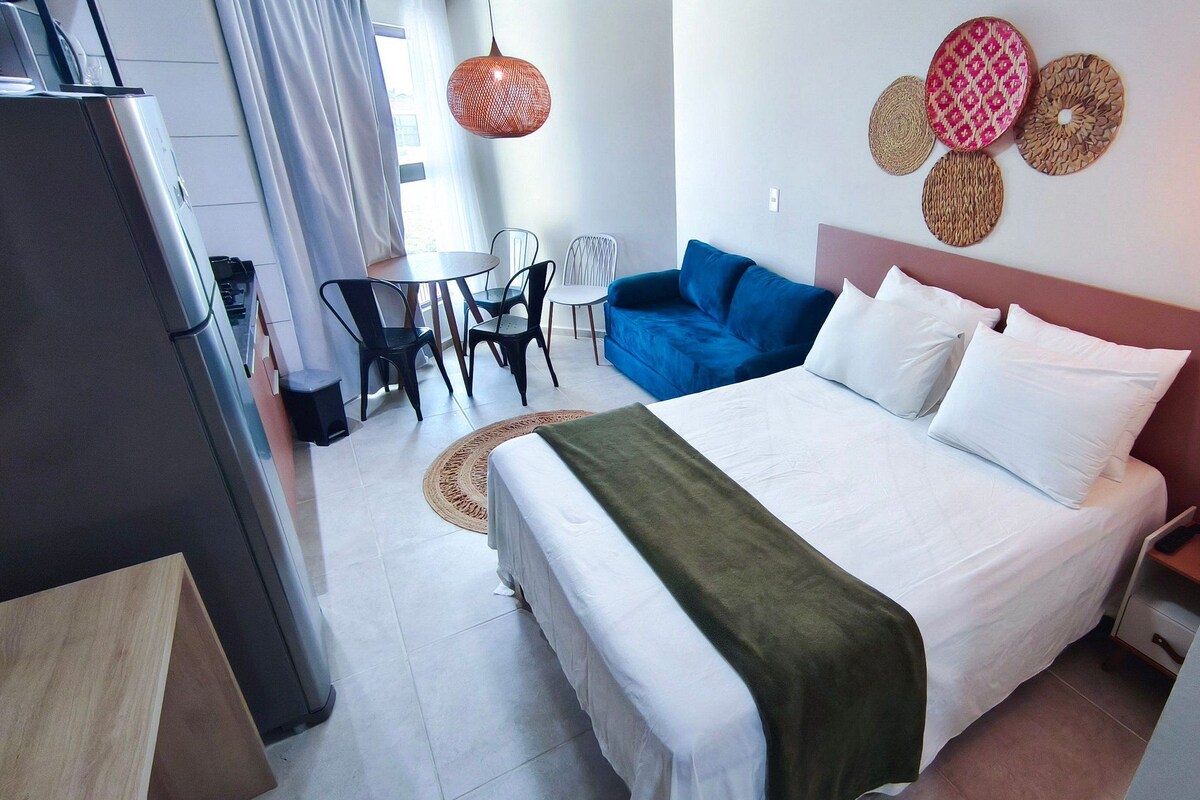 A hotel room with a bed, a blue sofa, a dining table with chairs, a small kitchen area, and decorative wall art.