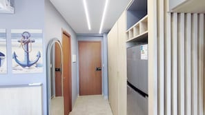 A hallway with a wooden door, a refrigerator, and a wall-mounted picture of an anchor. - Max Carneiros Suites by CTA (Tamandaré)