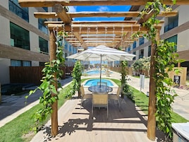 Uma área de estar ao ar livre com piscina, rodeada por pérgulas de madeira e vegetação.