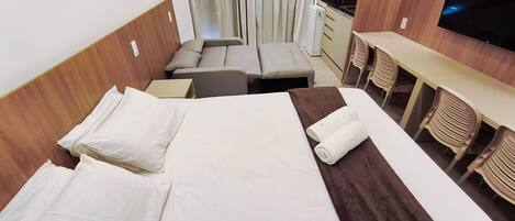 A hotel room with a bed, a small desk, a chair, a TV, and a kitchenette.