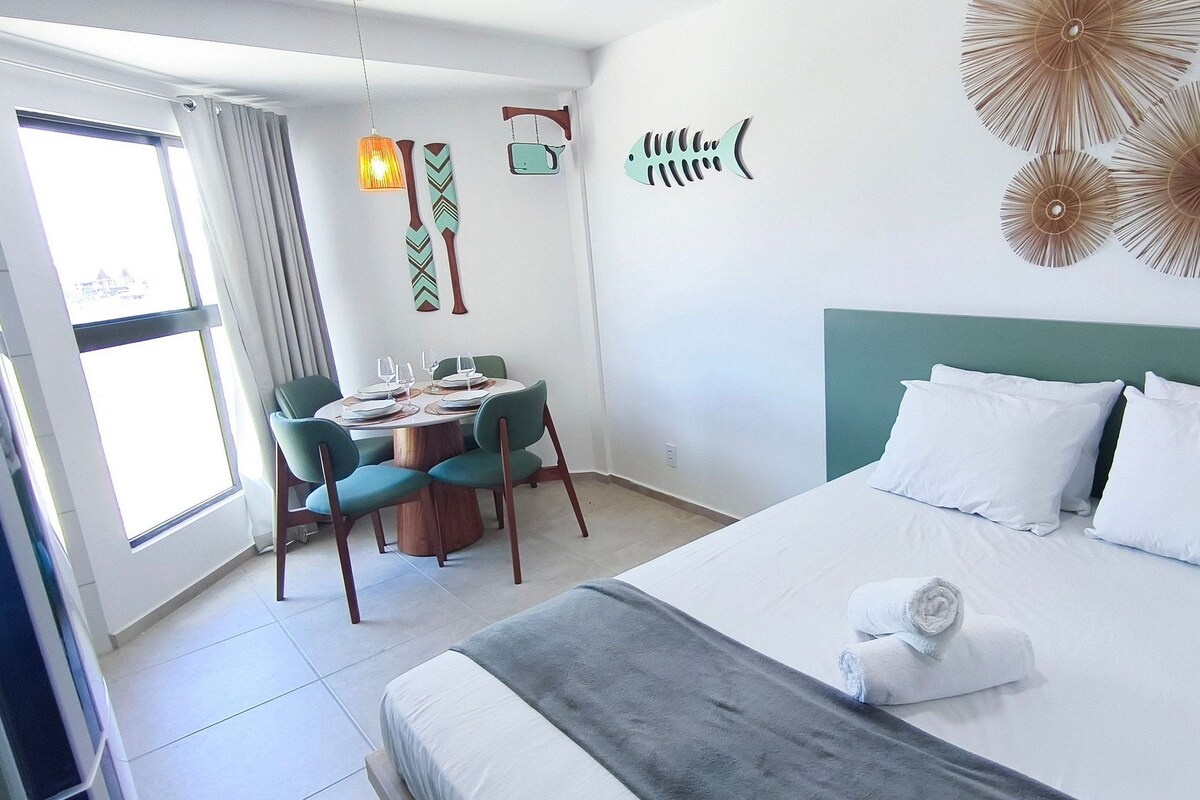 A hotel room with a bed, a dining table with chairs, and a view of the outside.