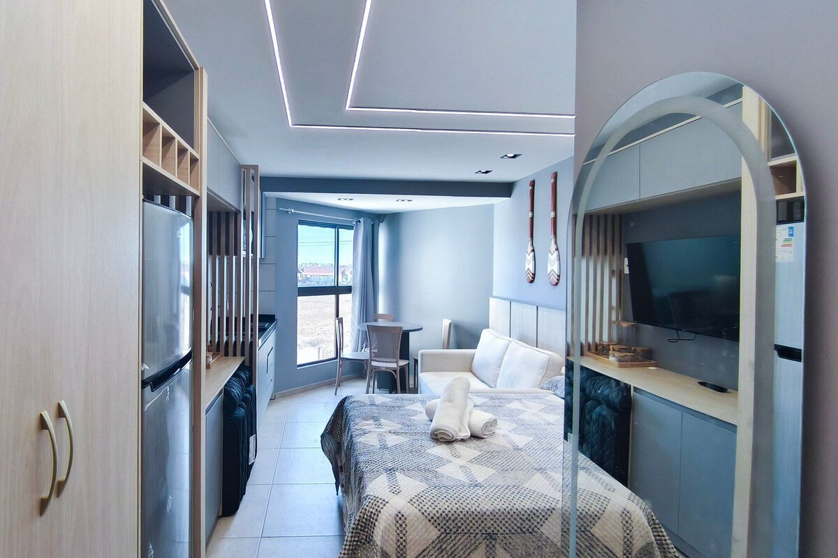 A modern bedroom with a bed, a TV, and a dining area with chairs.
