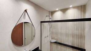 Ein modernes Badezimmer mit rundem Spiegel, einer Duschkabine aus Glas und einem Waschtisch mit schwarzem Rahmen.