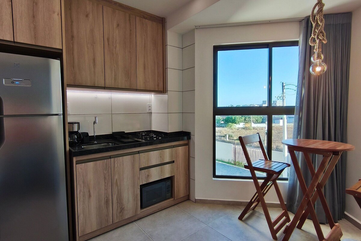 Une cuisine moderne avec des meubles en bois, un réfrigérateur en acier inoxydable, une cuisinière à gaz et un four à micro-ondes. On y trouve un coin repas avec une table et des chaises en bois, ainsi qu’une grande fenêtre donnant sur l’extérieur.