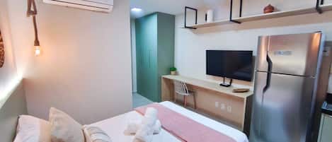 A hotel room with a bed, a desk, a television, and a refrigerator.