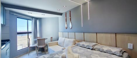 A modern hotel room with a large bed, a seating area with a table and chairs, a view through a large window, and a wall-mounted bat decoration.