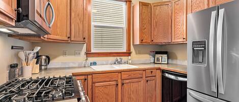 A kitchen with wooden cabinets, a stainless steel refrigerator, a gas stove, a window with blinds, and a microwave.