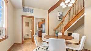 A dining area with a round wooden table, white upholstered chairs, and a staircase with wooden railings.