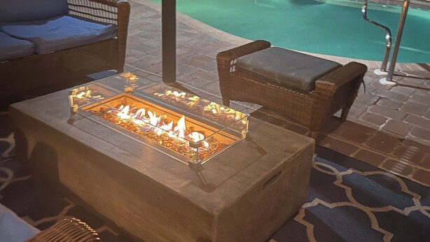 A poolside area with a fire pit table, wicker furniture, and a pool in the background. - Fantastic 3-bedroom house with private heated pool (Nokomis)