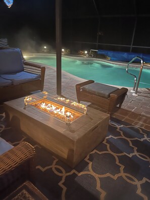 A poolside area with a fire pit table, wicker furniture, and a pool in the background. - Fantastic 3-bedroom house with private heated pool (Nokomis)