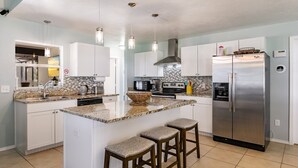 A modern kitchen with white cabinets, a stainless steel refrigerator, a granite countertop, and three bar stools. - Fantastic 3-bedroom house with private heated pool (Nokomis)