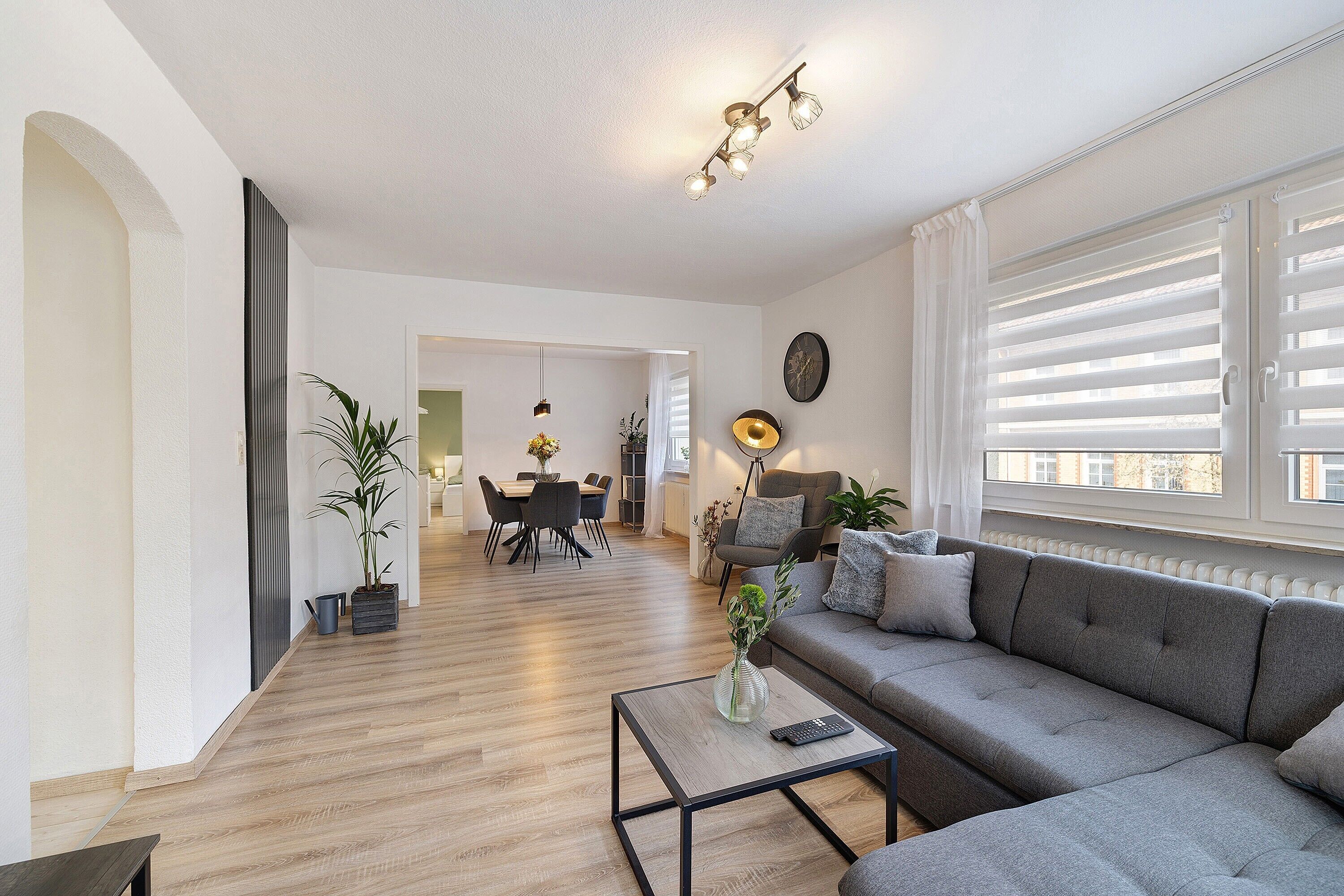 En moderne stue med sofa, sofabord og et spiseområde i baggrunden.