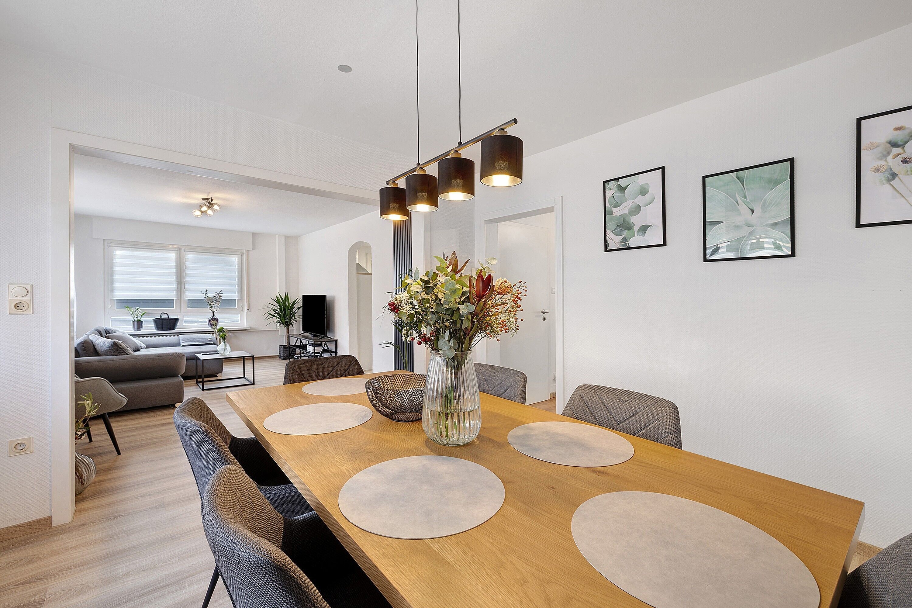 A modern dining area with a wooden table, round placemats, and a vase with flowers.