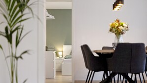 Un comedor moderno con una mesa, sillas, un florero con flores y una cama al fondo.