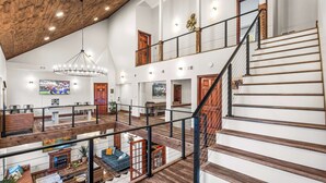 A spacious interior with a high ceiling, wooden beams, a staircase, and a mezzanine level. - Skylark Pines-Luxury 8BR/5.5BA Massanutten Retreat (McGaheysville)