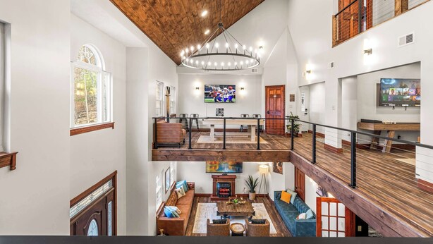 A spacious multi-level living area with a wooden ceiling, a central chandelier, a fireplace, and a television on the upper level. - Skylark Pines-Luxury 8BR/5.5BA Massanutten Retreat (McGaheysville)