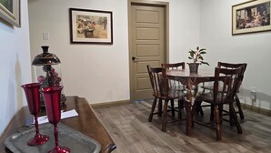 A dining area with a wooden table, chairs, a potted plant, and framed pictures on the walls.