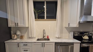 A modern kitchen with white cabinets, a stainless steel sink, a coffee maker, a kettle, and a dishwasher.