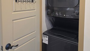 A laundry room with a black washer and dryer, a hanging rack with laundry detergent, and a coat rack.