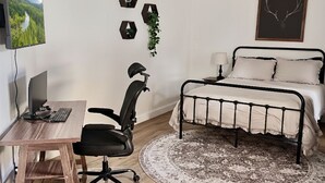Makuuhuone, jossa on sänky, työpöytä tietokoneella, tuoli, matto ja seinäkoristeita.