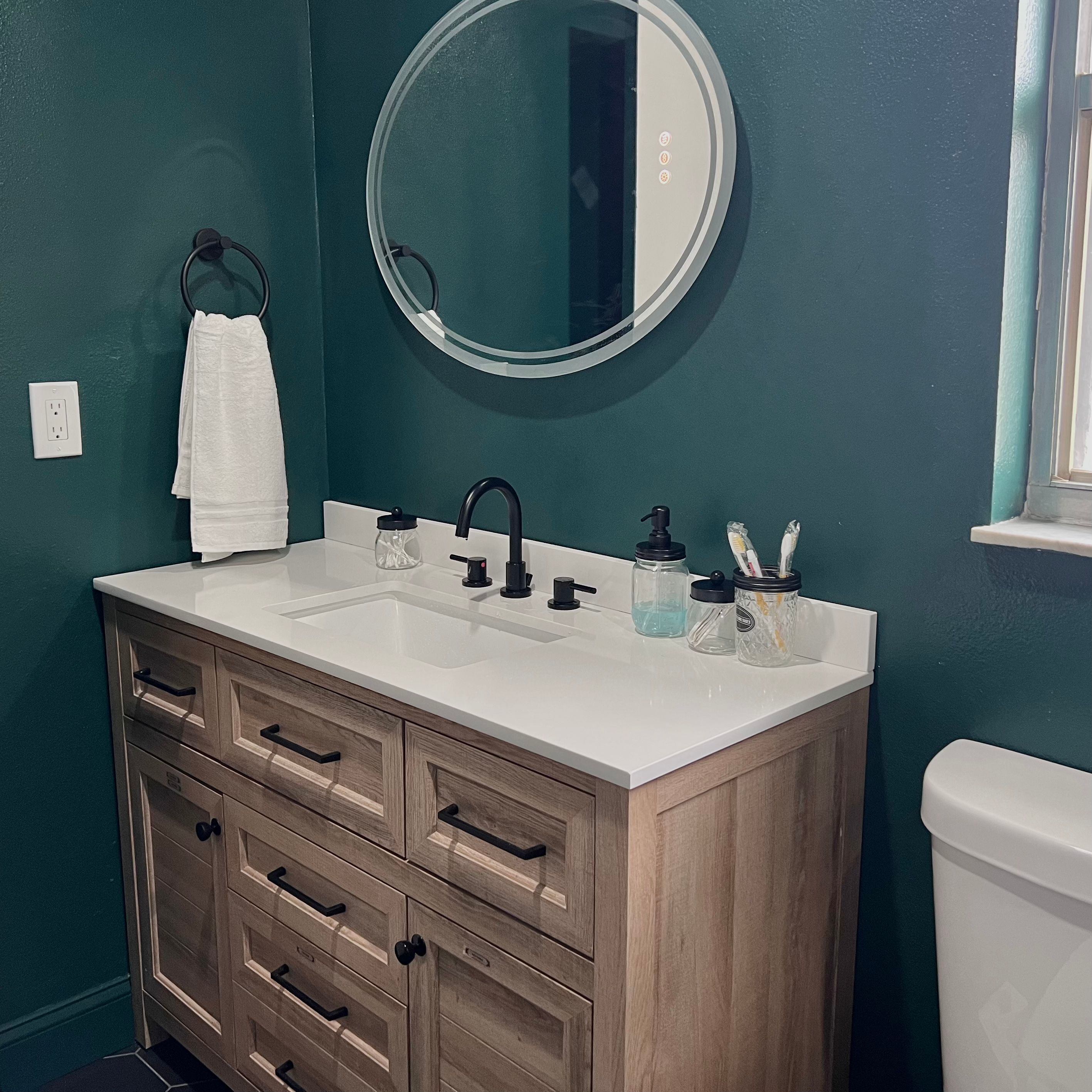 Une salle de bain avec un lavabo blanc, un robinet foncé et un meuble en bois en dessous.