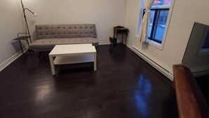 A living room with a sofa, a white coffee table, a floor lamp, a small table, and a TV on a stand. - Montreal Mile-Ex close to MIL (Montréal)