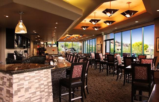 A spacious indoor area with a bar, multiple seating arrangements, and large windows offering a view.