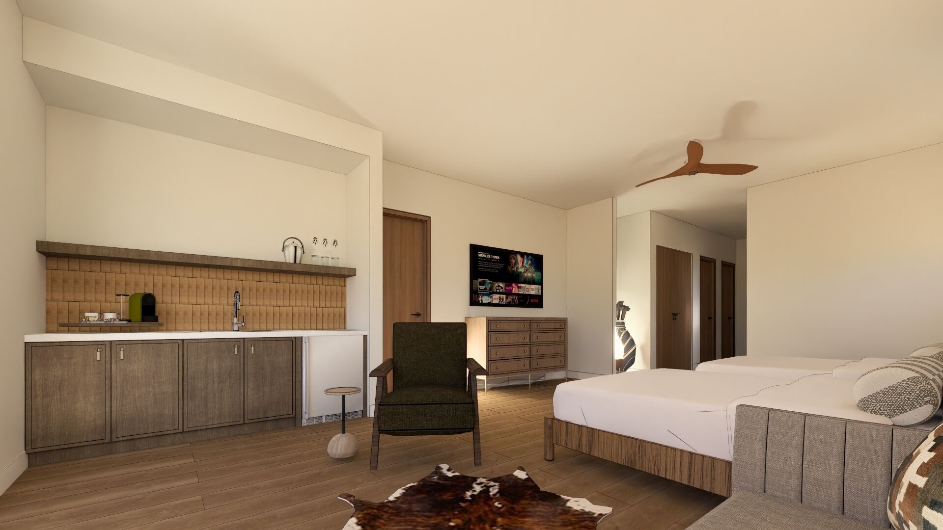 A modern hotel room with a kitchenette, a bed, a chair, a TV, and a ceiling fan.
