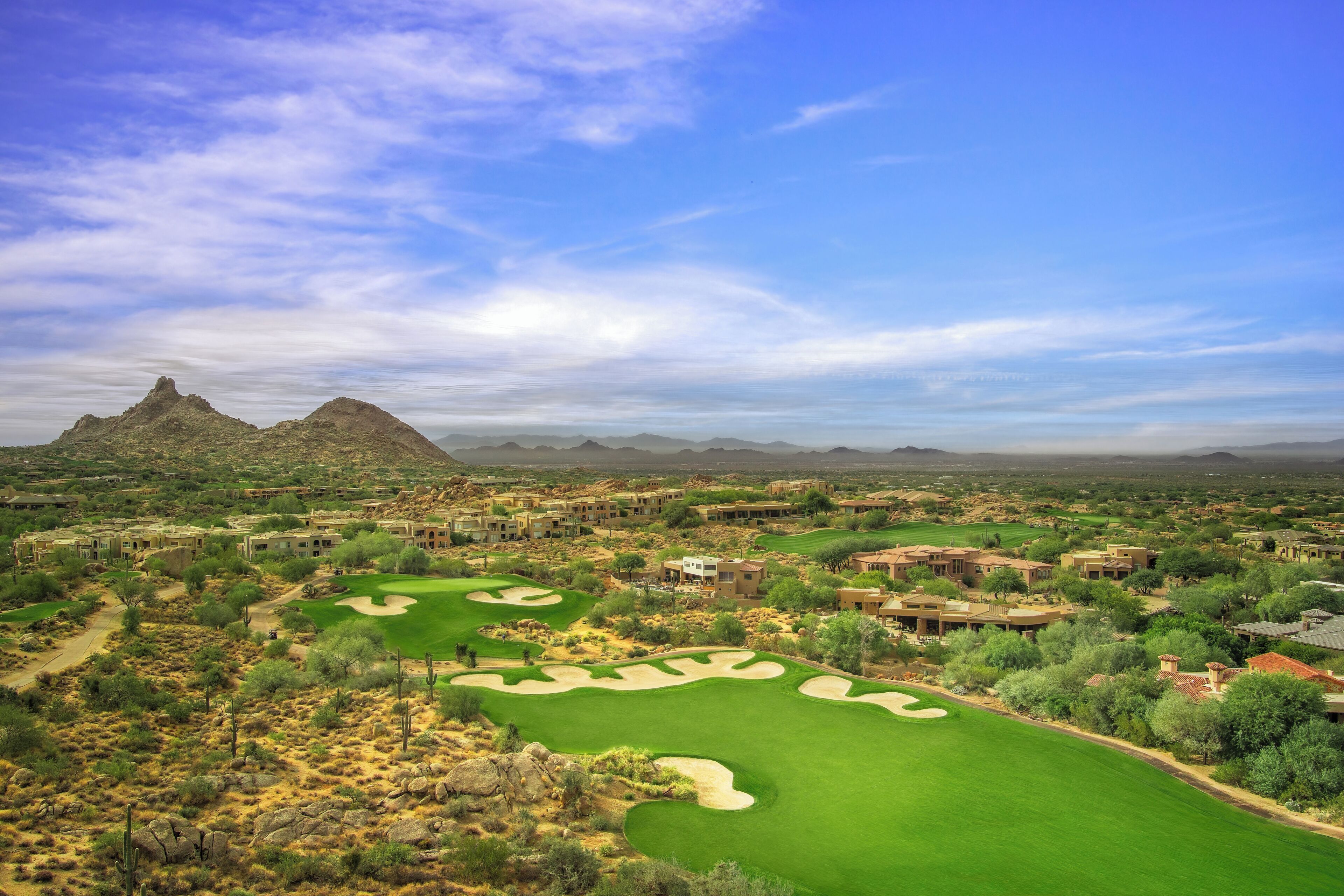 A golf course with bunkers, a desert landscape, and distant mountains.