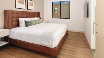 A hotel room with a large bed, a bedside table, a nightstand, a wall-mounted lamp, and two framed pictures.
