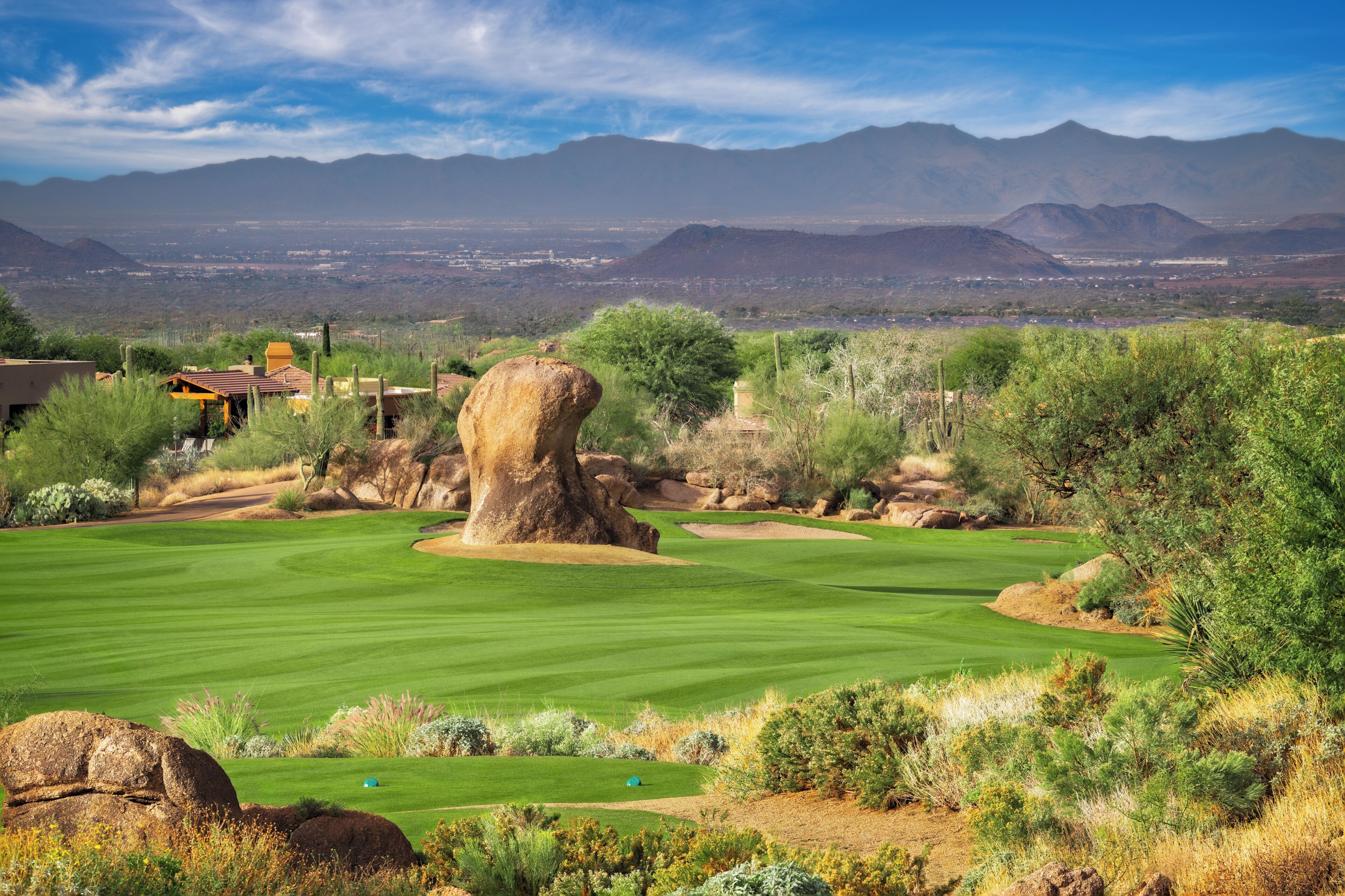 A golf course with a large rock, cacti, and mountains in the background.