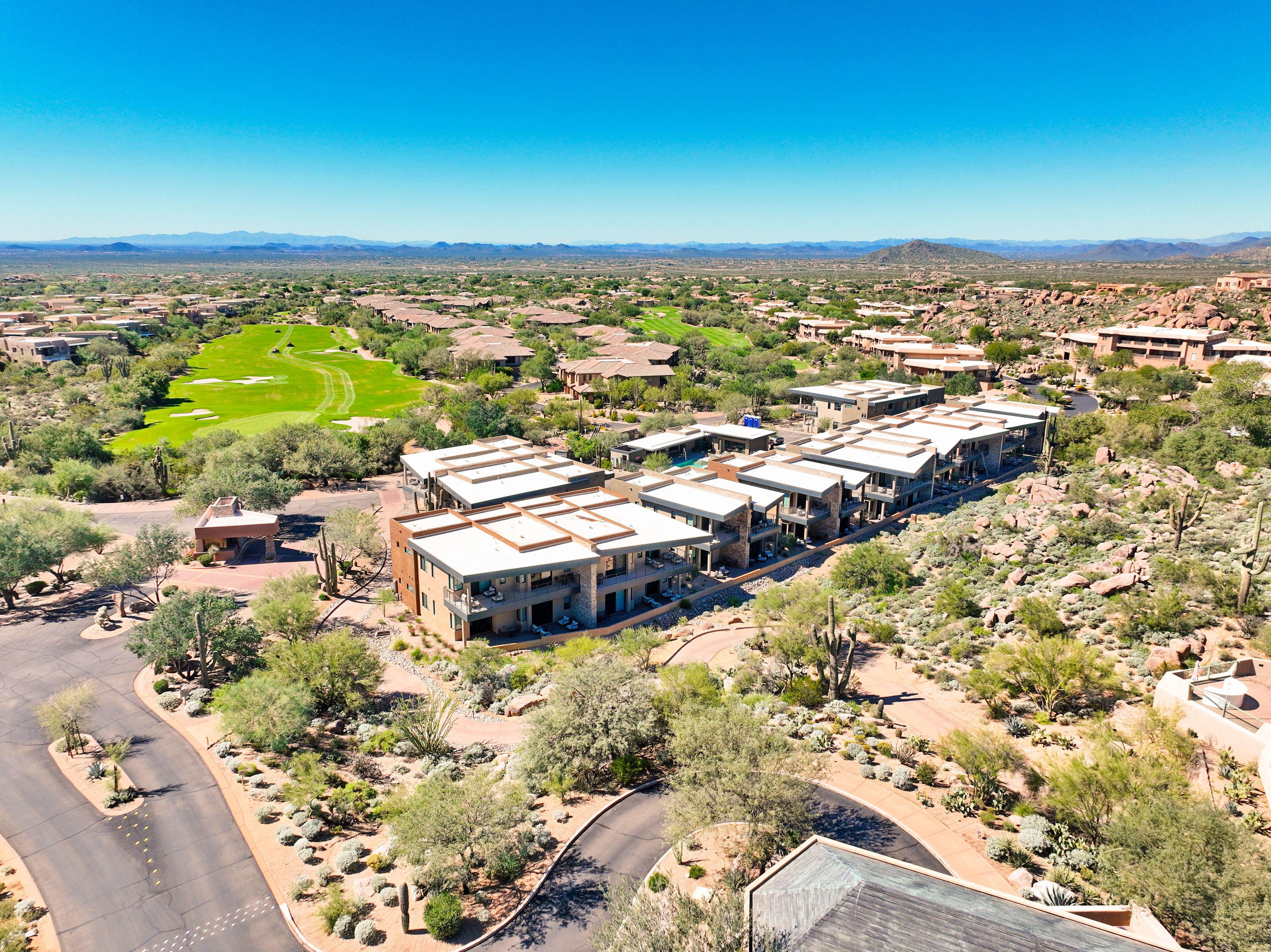 A modern multi-story hotel with a flat roof, surrounded by desert vegetation and a golf course.