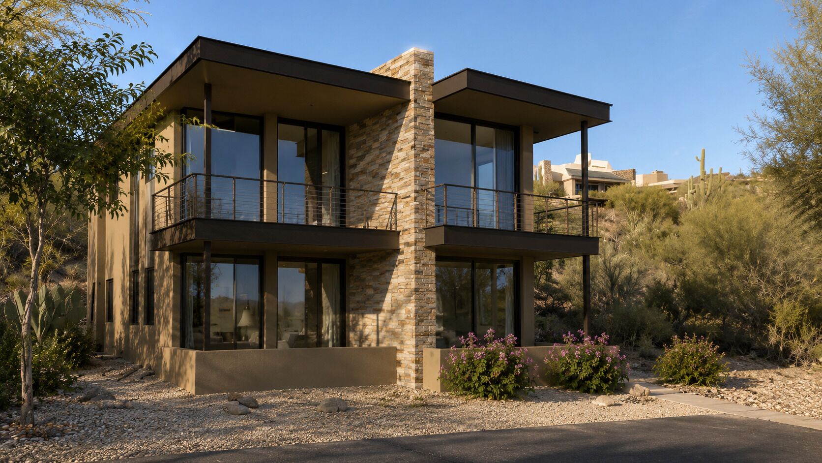A modern two-story building with large windows, a stone chimney, and a landscaped garden with cacti and shrubs.