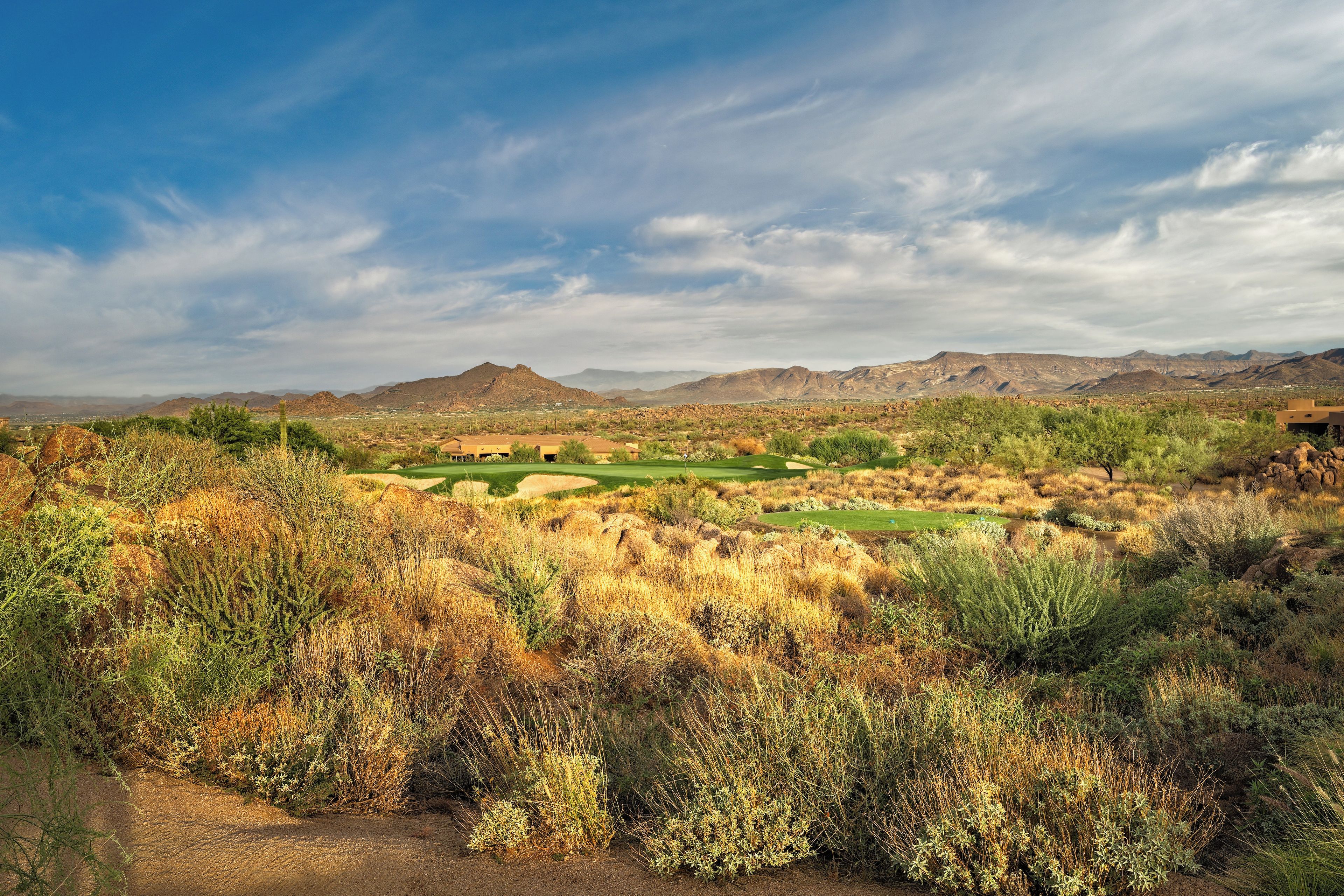 A desert landscape with a golf course, mountains in the background, and sparse vegetation.