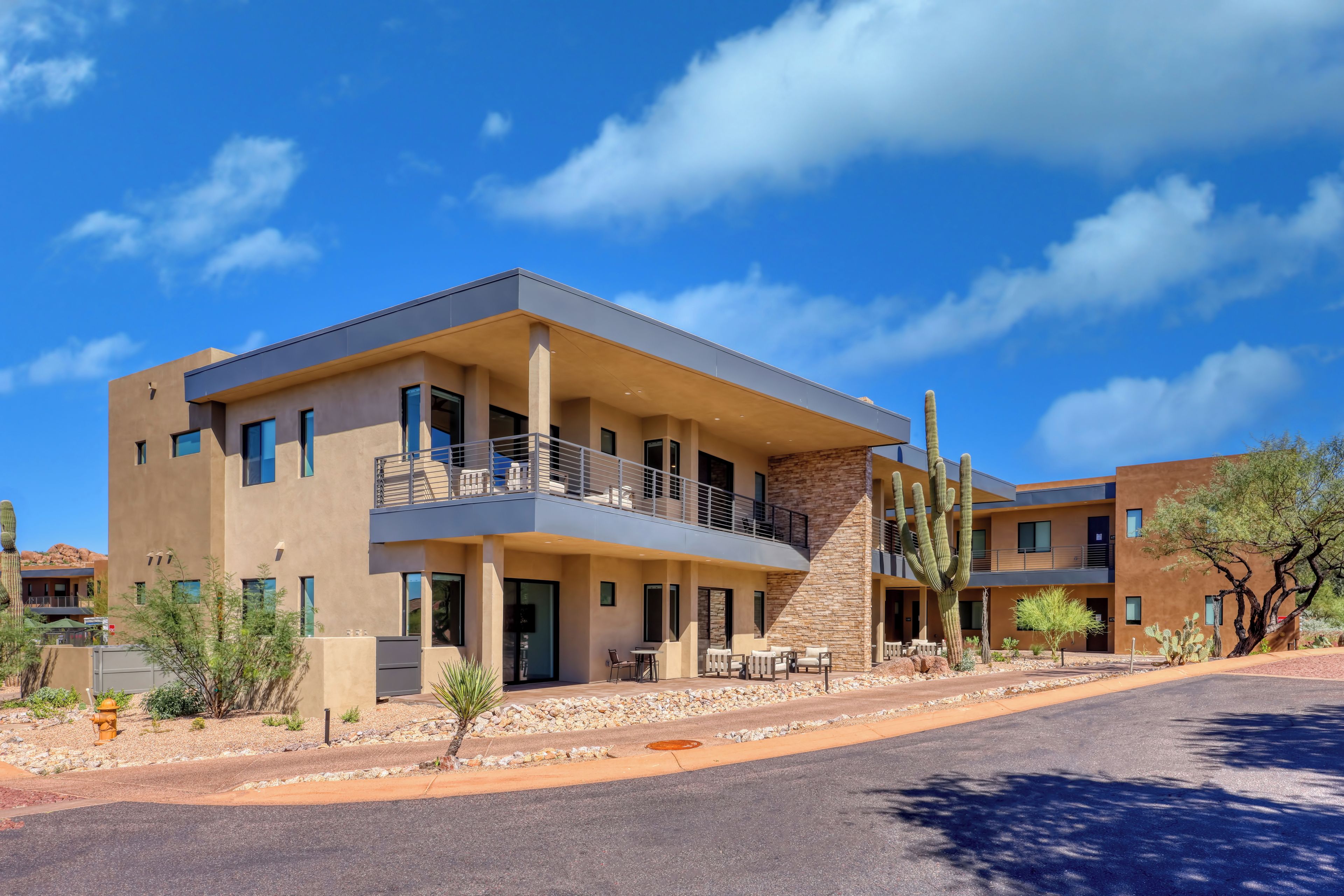 A modern multi-story hotel with a flat roof, balconies, and a desert garden with cacti.