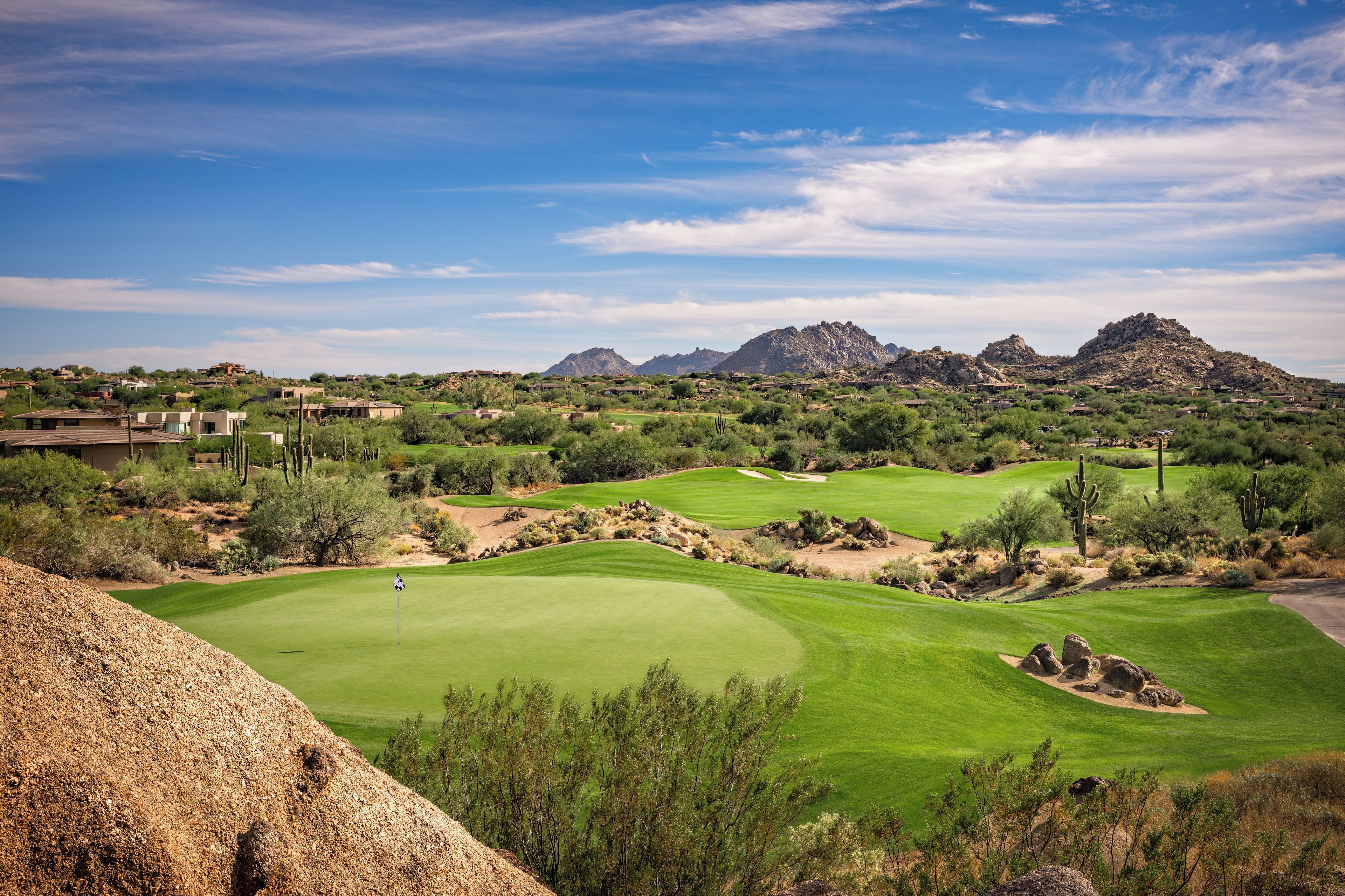 Un campo da golf con cielo sereno, fairway verdi e montagne rocciose sullo sfondo.